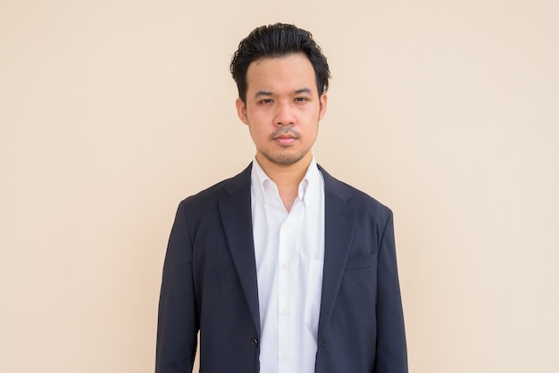 Portret van een Aziatische zakenman die een pak draagt tegen een effen achtergrond