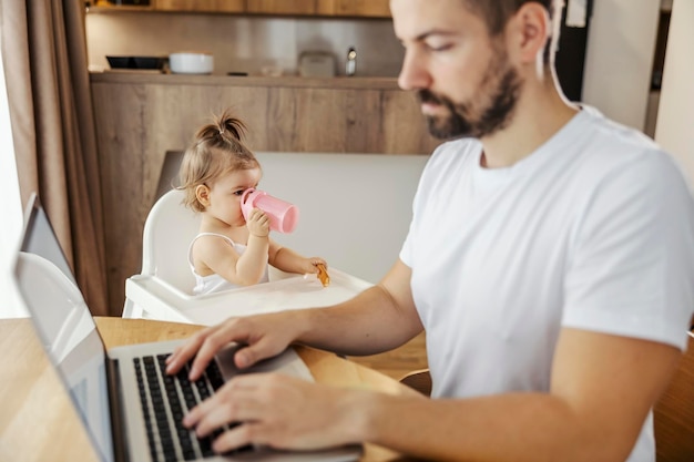 Portret van een babymeisje dat achteloos een water drinkt terwijl haar vader zijn werk afmaakt