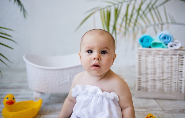 Portret van een babymeisje in een badhanddoek die naast een babybadje zit. kinderopvang