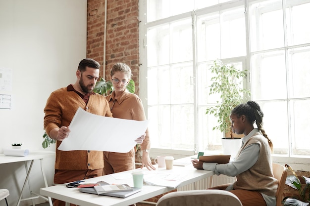 Portret van een bebaarde man die projectplannen vasthoudt terwijl hij met een creatief ontwerpteam in de studio werkt, kopieer ruimte