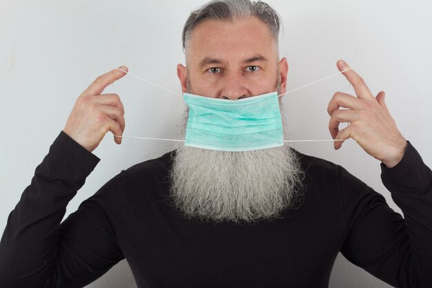 Portret van een bebaarde man van middelbare leeftijd in een medisch masker. Een concept van het gevaar van coronavirus voor ouderen.