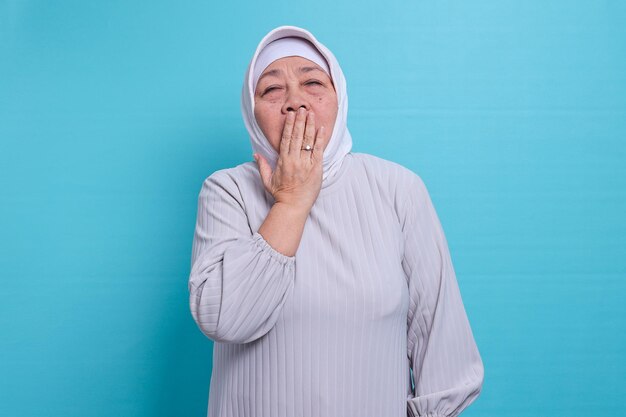 Portret van een bejaarde vrouw die op een blauwe achtergrond gaapt