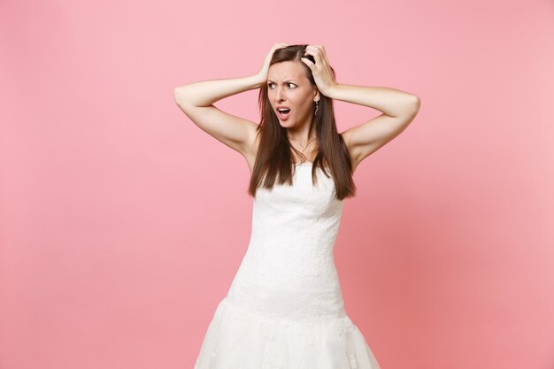 Portret van een bezorgde, geschokte vrouw in een witte jurk die opzij staat en zich vastklampt aan het hoofd