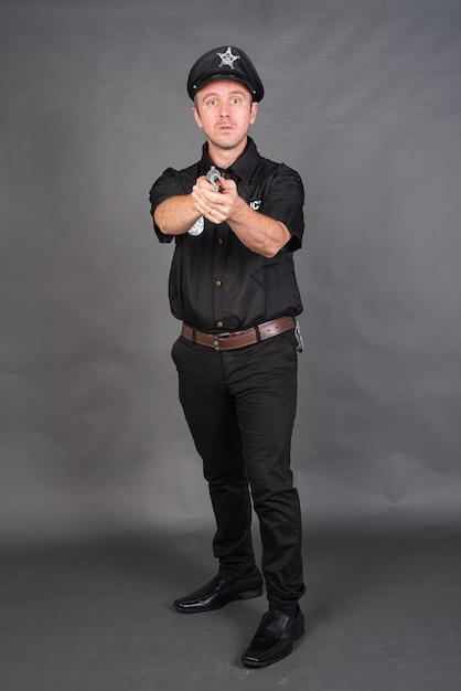 Portret van een blanke man in een politieuniform tegen een grijze achtergrond van een studio.