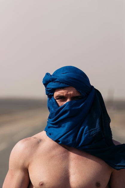 Portret van een blanke man met een tulband die naar de camera in de woestijn kijkt.