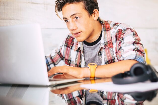 Foto portret van een blanke tiener met een koptelefoon die naar het laptopscherm staart tijdens het spelen van computerspelletjes, chatten op internet of het bekijken van video's. - afbeelding