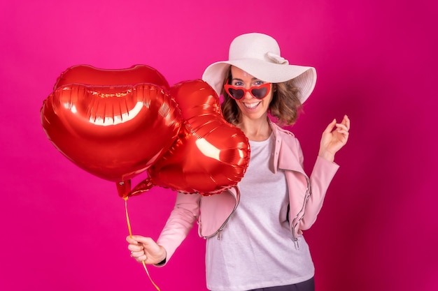 Portret van een blanke vrouw die plezier heeft met dansen met een witte hoed in een nachtclub met een paar hartballonnen roze achtergrond