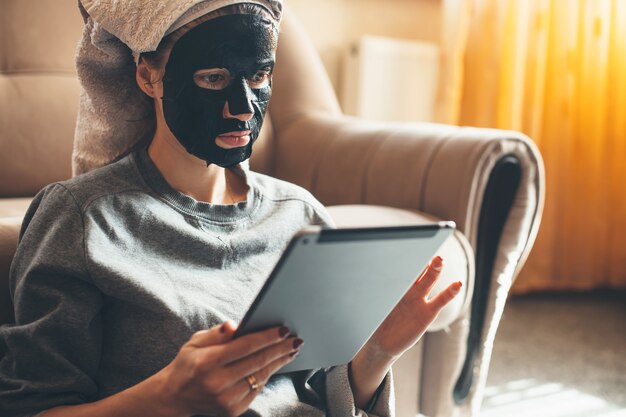 Portret van een blanke vrouw die thuis een zwart masker draagt en een tablet op de vloer gebruikt, close-up