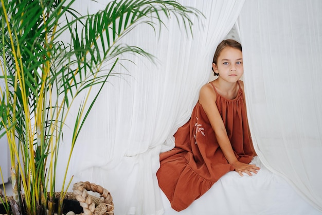 Foto portret van een blauwogen meisje in een zomerjurk die op het bed zit