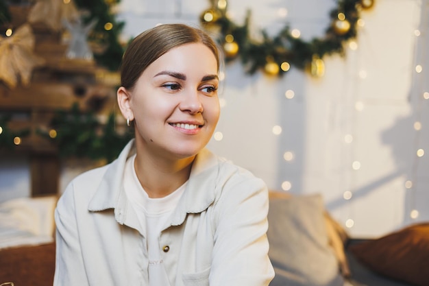 Portret van een blij lachende vrouw tegen de achtergrond van nieuwjaarsversieringen De vrouw is blij met de kerstvakantie Nieuwjaarssfeer thuis