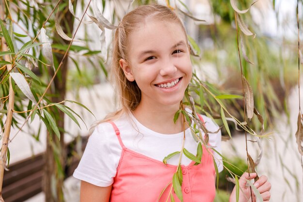 Portret van een blond, lachend tienermeisje in de buurt van een boom in de zomer.