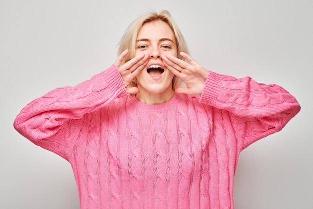 Foto portret van een blond meisje dat luid schreeuwt met handen nieuws palmen gevouwen als megafoon geïsoleerd op witte achtergrond