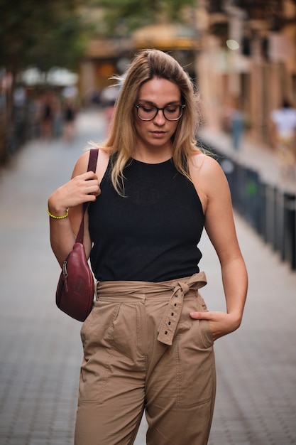 Foto portret van een blond meisje met een bril die poseert voor een fotoshoot op een straat in de stad barcelona.