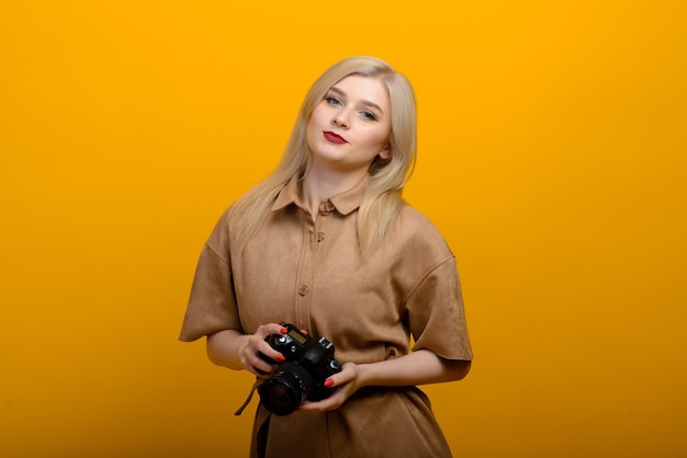 Portret van een blond meisje met een camera in de hand op een gele achtergrond. Geïsoleerde studio.