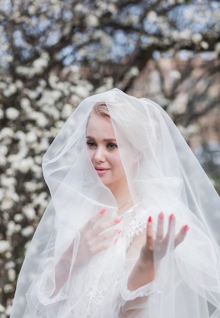 Portret van een blonde bruid met een sluier in een bloeiende lentepark