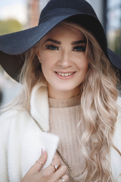 Foto portret van een blonde dame in een zwarte hoed, lang haar, beige jas.