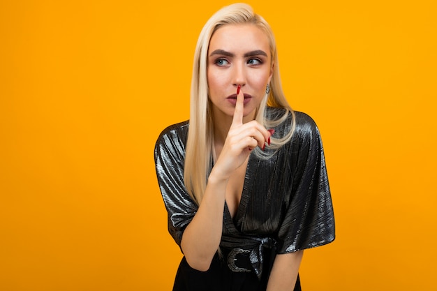 portret van een blonde jonge vrouw die vraagt om rustiger te zijn op een gele studio-oppervlak