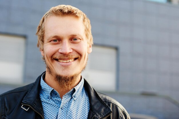 Portret van een blonde man met een baard en leren jas op de achtergrond van het gebouw