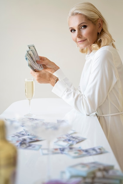 Foto portret van een blonde rijke vrouw van middelbare leeftijd met champagneglas en bankbiljetten