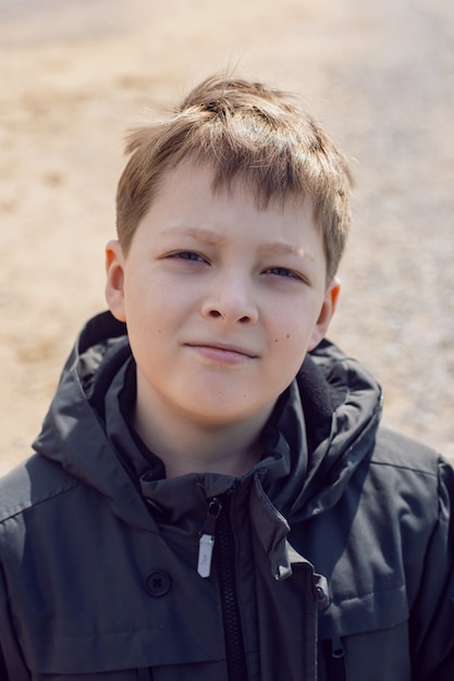 Foto portret van een blonde tiener in een zwarte jas op straat