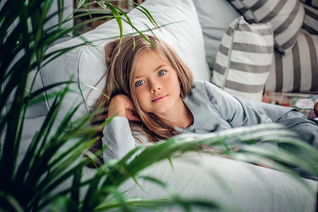 Portret van een blonde tienermeisje liggend op een coach in een kamer met groene planten.