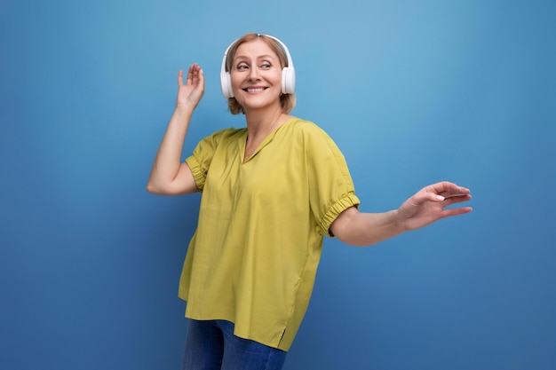 Portret van een blonde volwassen vrouw met een gadget om naar liedjes op een studioachtergrond te luisteren