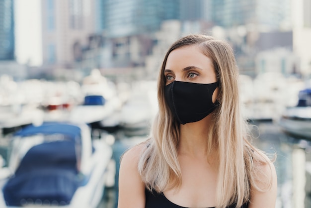 Portret van een blonde vrouw die beschermend gezichtsmasker van zwarte kleur draagt. Nieuw normaal concept