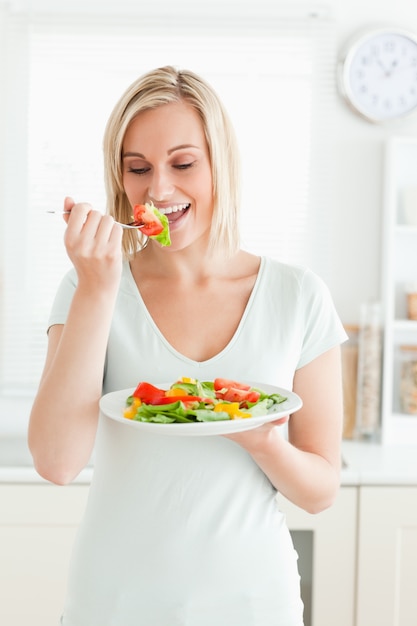 Portret van een blonde vrouw die van gemengde salade geniet