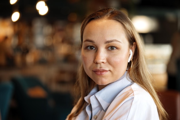 Portret van een blonde vrouw in wit overhemd zittend in café