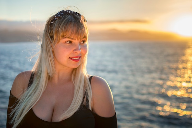 Portret van een blonde vrouw met de zee en verlicht door de avondzon.