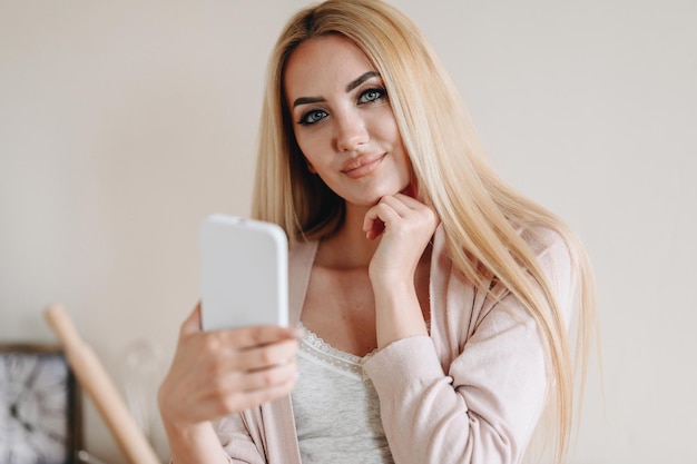Portret van een blonde vrouw met lang haar en expressieve make-up vrouw houdt telefoon in haar handen