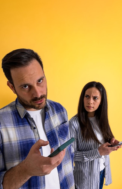 Portret van een boze en serieuze vrouw die frustrerend kijkt naar vriendjesberichten via een smartphone die over een gele achtergrond is geïsoleerd