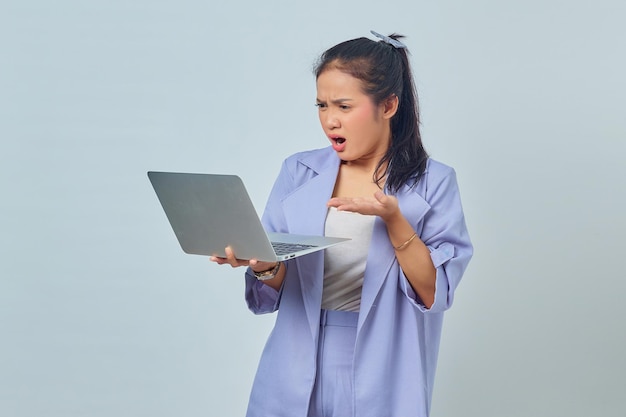 Portret van een boze jonge Aziatische vrouw die kopieerruimte in handpalmen toont en een laptop vasthoudt die op een witte achtergrond wordt geïsoleerd