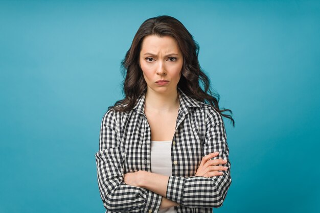 Portret van een boze jonge vrouw die over een geïsoleerde blauwe achtergrond staat en naar de camera kijkt