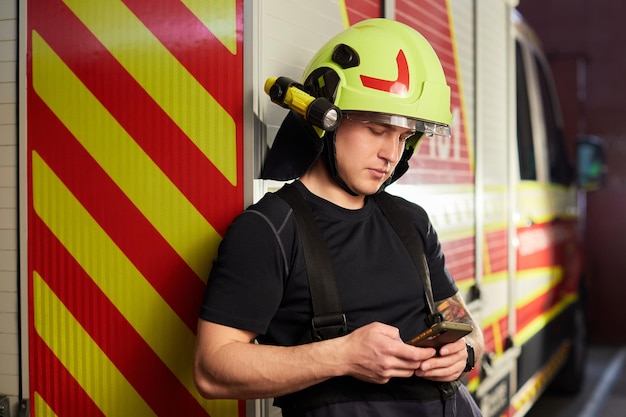 Portret van een brandweerman die voor een brandweerwagen staat Brandweerman die een smartphone gebruikt