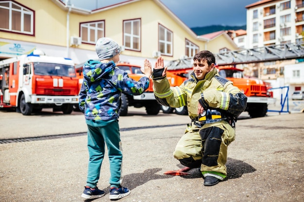 Portret van een brandweerman met een kind dat tegen de achtergrond van brandweerwagens staat Kinderdromen