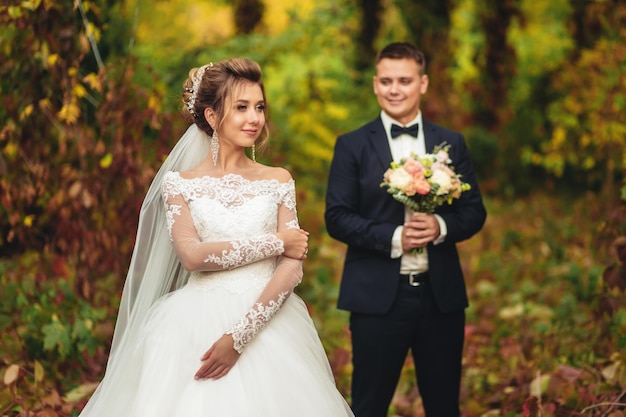 Portret van een bruid in een herfstpark De bruidegom kijkt met tederheid naar de bruid op de achtergrond