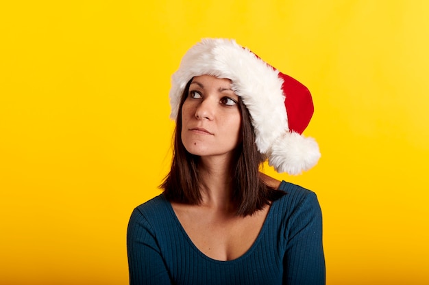 Portret van een brunette meisje in een kerstman hoed met gele achtergrond