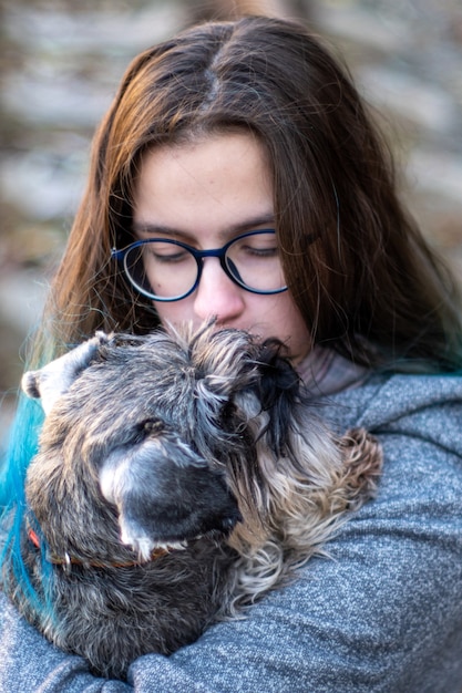 Portret van een brunette meisje met een bril houdt een puppy, hond, dwergschnauzer in haar armen. Favoriete huisdieren concept.