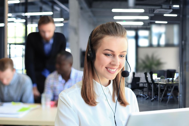 Portret van een callcentermedewerker vergezeld door haar team Glimlachende medewerker van de klantenservice op het werk