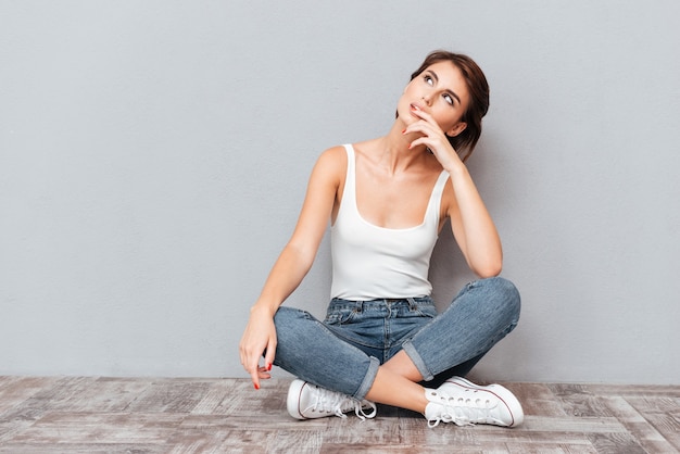 Portret van een casual gelukkig afvragend vrouw zittend op de vloer op een grijze achtergrond