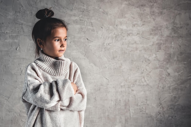 Portret van een charmant klein meisje in beige trui op grijze achtergrond
