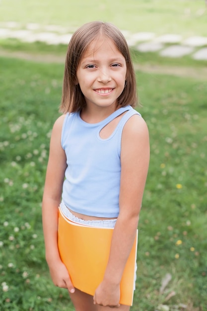 Portret van een charmant meisje van 8-10 jaar oud in een t-shirt en korte broek met een geel boek in haar handen, op een zomerse groene weide, gefilterde afbeelding. opleiding