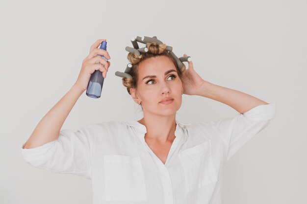 Portret van een charmante jonge vrouw in krulspelden met spray in haar handen