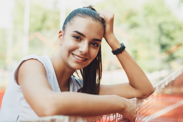 Portret van een charmante jonge vrouw met zwart haar die tijdens het rusten na het doen van ochtendsport buiten glimlachen.