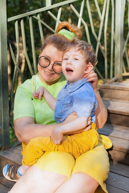 Portret van een charmante kleine gehandicapte jongen liggend in de armen van zijn liefhebbende moeder op het groene gras in het park. onbekwaamheid. Moeders liefde. Familie ondersteuning.
