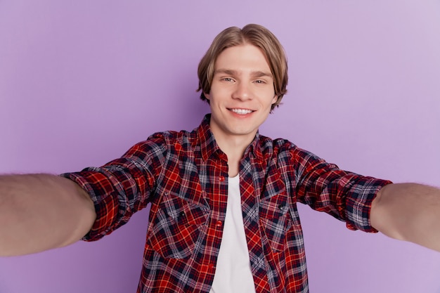 Portret van een charmante knappe jongen neemt selfie, een stralende glimlach op een violette achtergrond