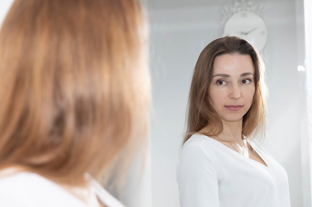 Foto portret van een charmante mooie brunette blanke vrouw van 40 jaar die naar de spiegel kijkt en gezond glimlacht.