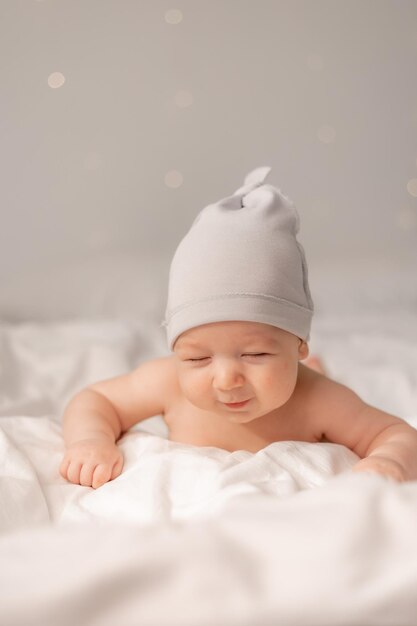Portret van een charmante vrolijke baby met blauwe ogen in een witte muts liggend op zijn buik op wit beddengoed. ruimte voor tekst. Hoge kwaliteit foto