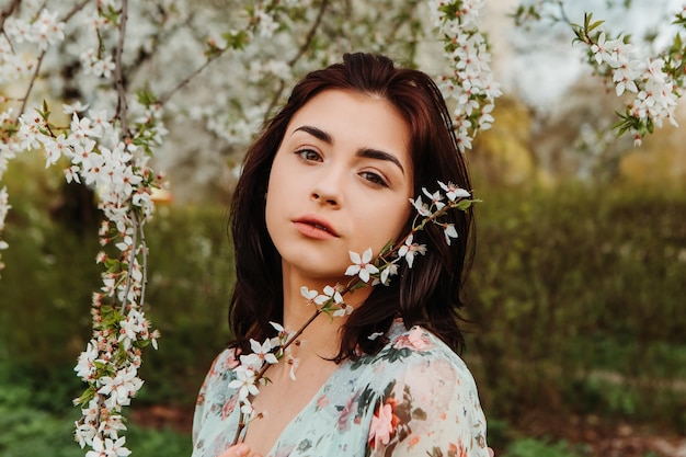 Portret van een charmante vrouw die zich voordeed in de buurt van appel-kersenboom bloeit bloeiende bloemen in de tuin